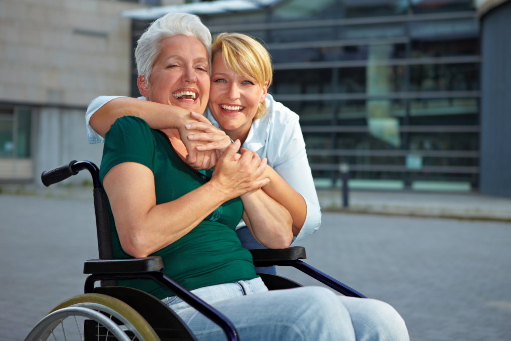 A caregiver hugging an elderly sitting on a wheelchair
